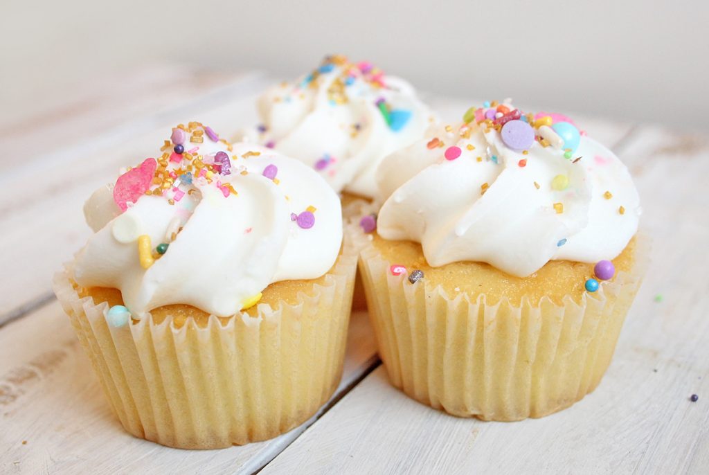 Trois cupcakes sur une table en bois blanc